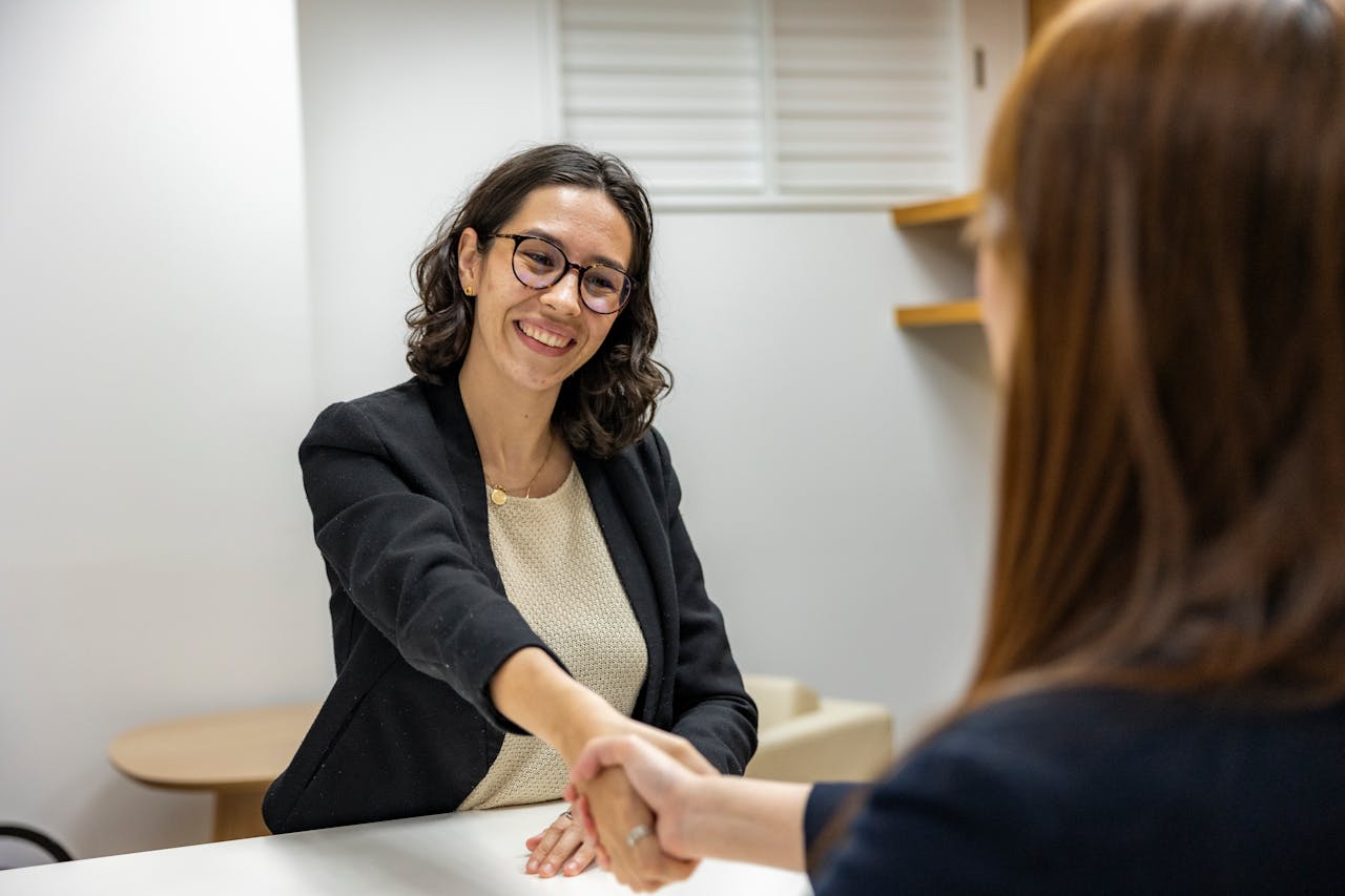 about-img Businesswomen shaking hands in an office, representing a successful job interview or partnership.