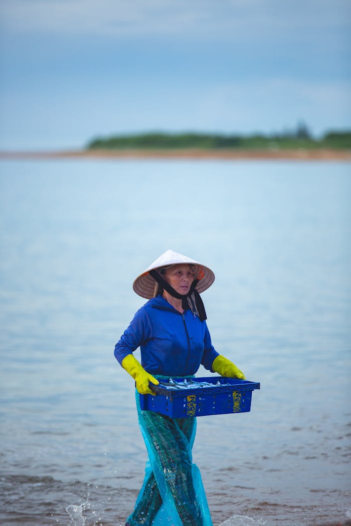 services-01 A fisherwoman in traditional attire carrying a seafood basket by the sea.
