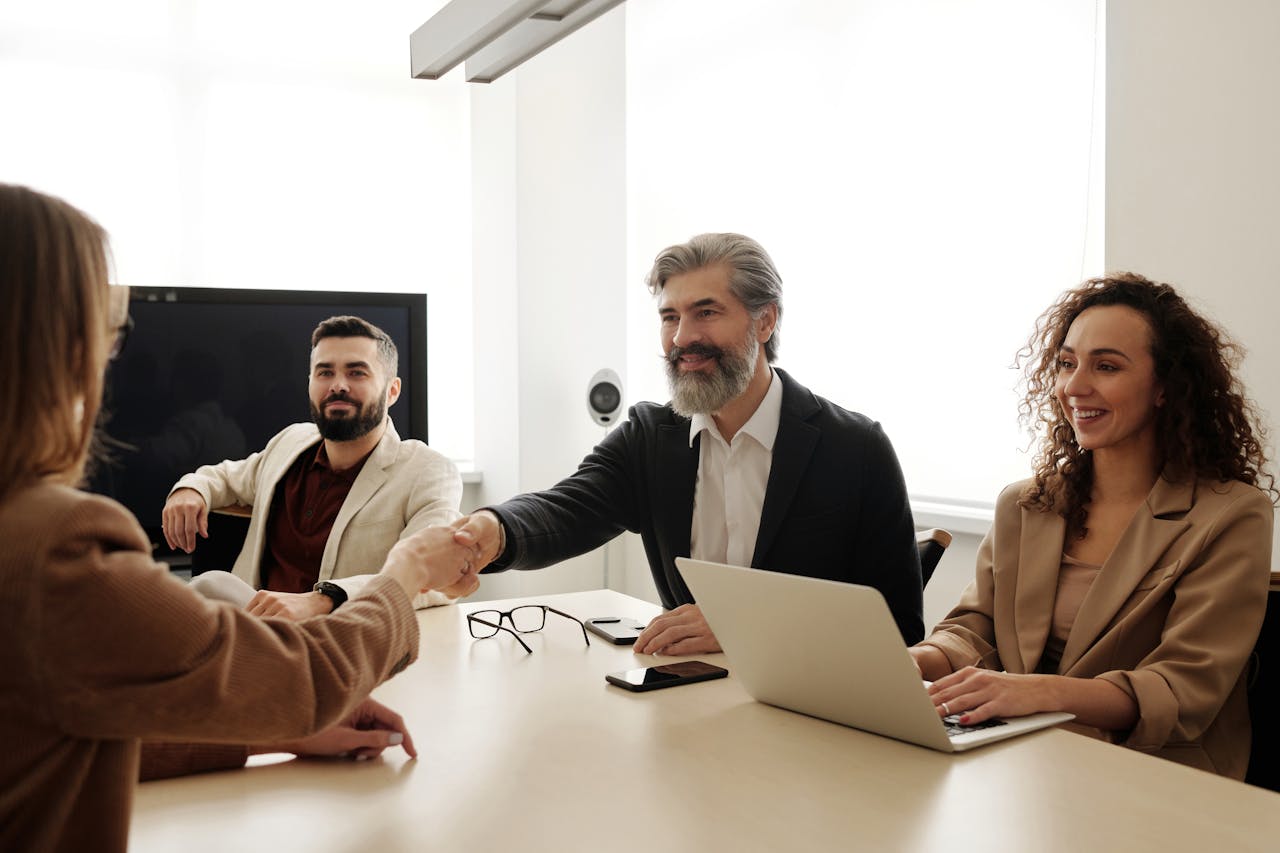 services-02 A group of business professionals shake hands during a meeting in a modern office setting.