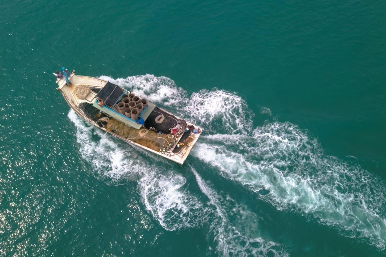 Drone view of boat with open deck and fishing equipment floating on calm sea at daytime