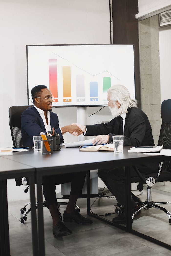 services-03 Two diverse businessmen in suits shaking hands over a desk in a modern office.